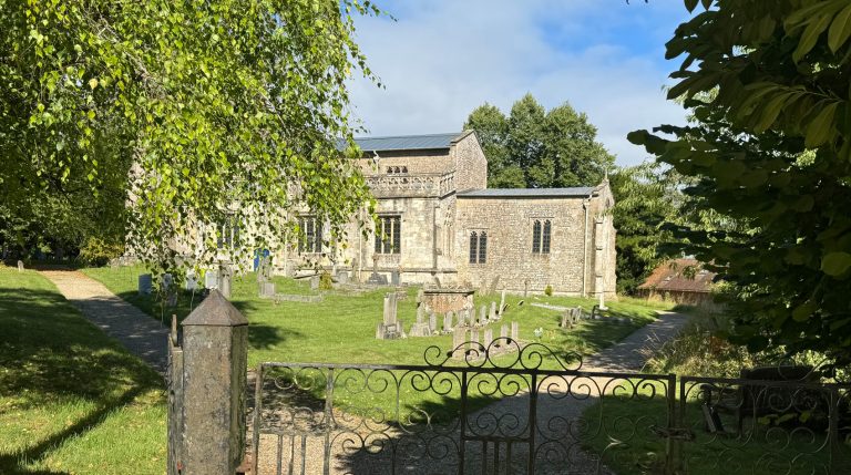 Historic stone church viewed through churchyard gate with gravestones and trees