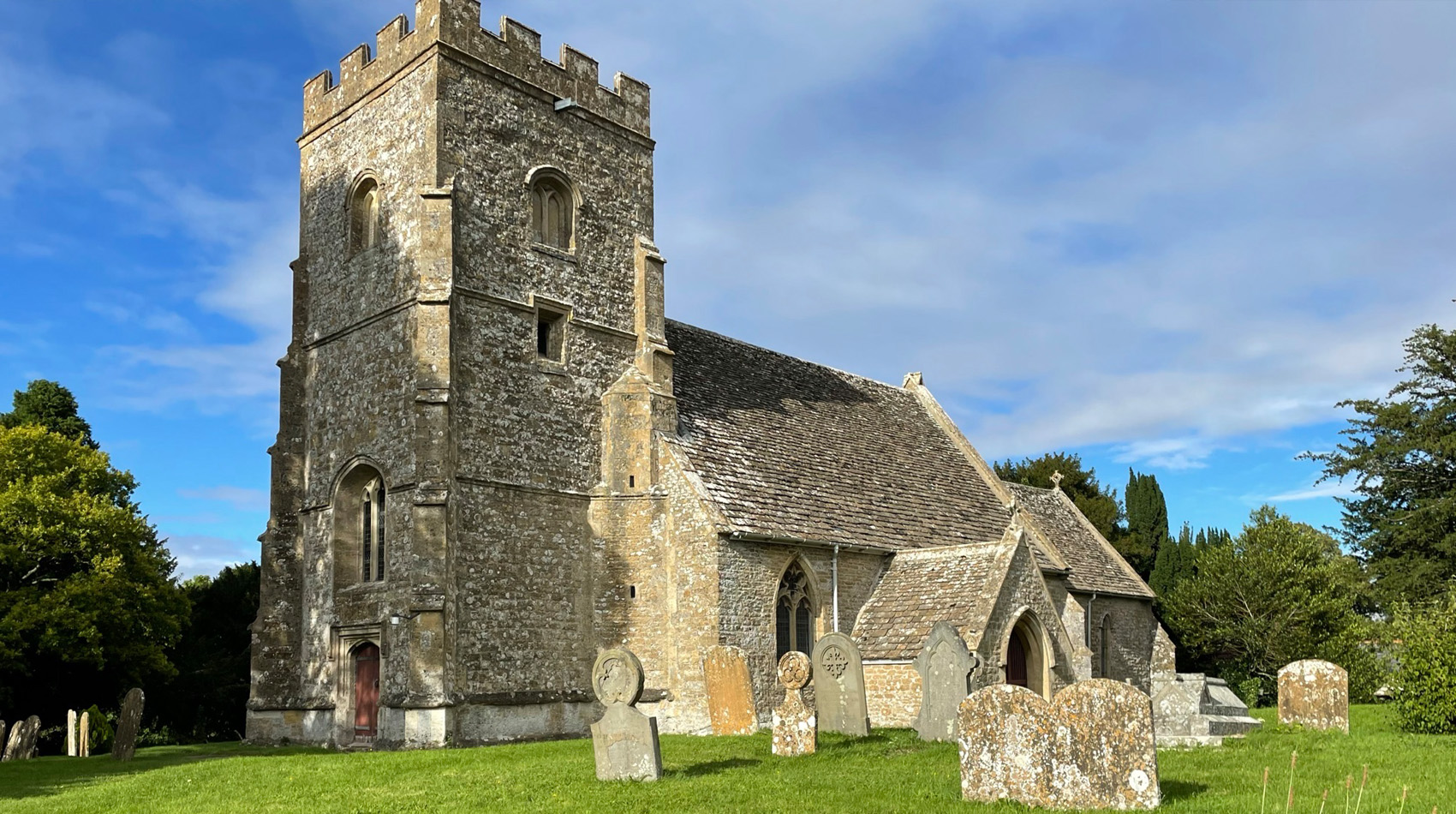 Historic stone church with tower and gravestones in churchyard under blue sky