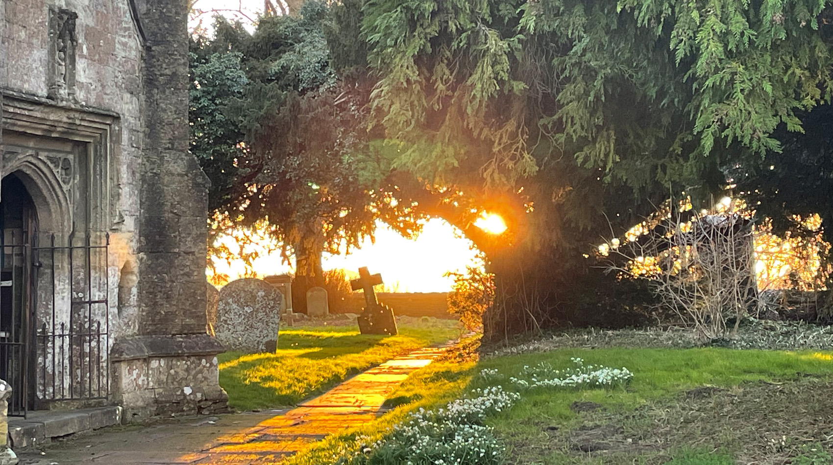 Sunset over churchyard with gravestones and stone path beside historic church